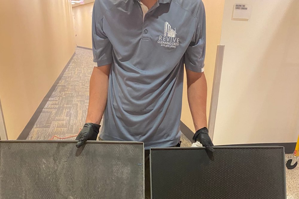 A Revive Cleaning Crew technician holding two air filter panels clogged with grey dust