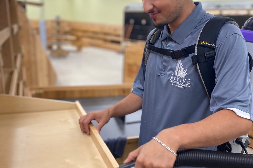 A Revive Cleaning Crew technician vacuuming sawdust from a newly built timber display unit with a backpack vacuum