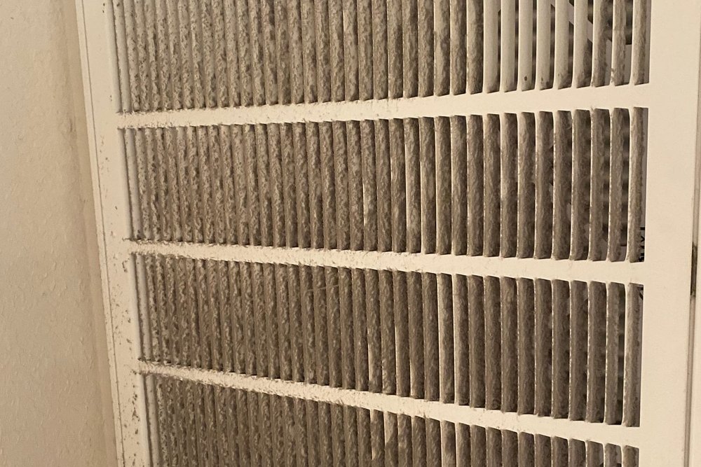 A return air grille heavily coated with grey dust and debris before cleaning