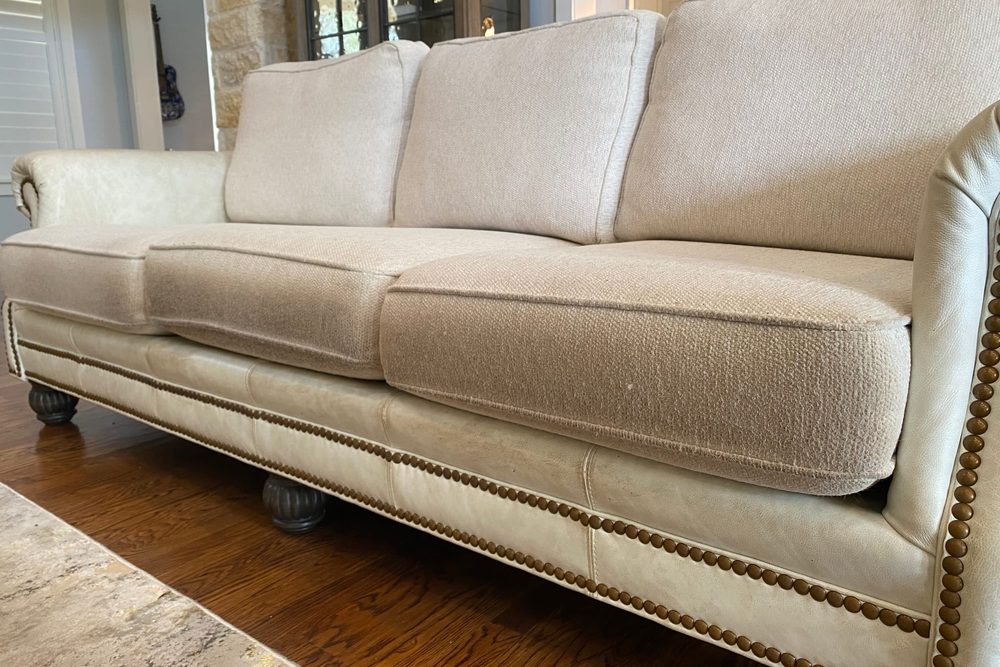 A cream fabric sofa with nailhead trim, cleaned, in a living room with wood floors